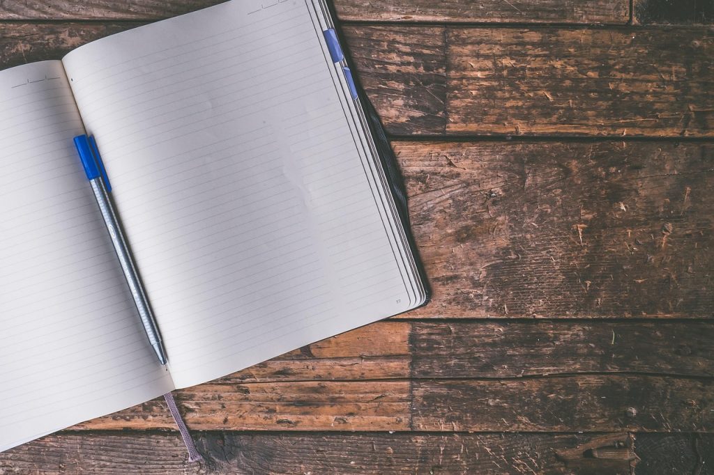An open lined notebook with a blue pen on a rustic wooden table.