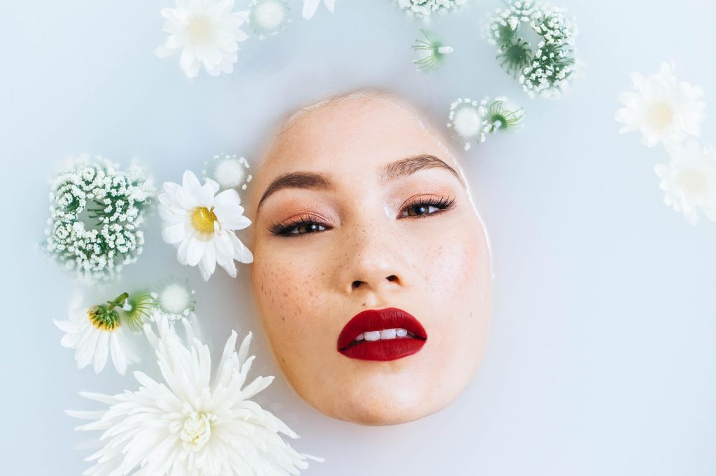 A woman's face surrounded by white flowers in a milky bath.