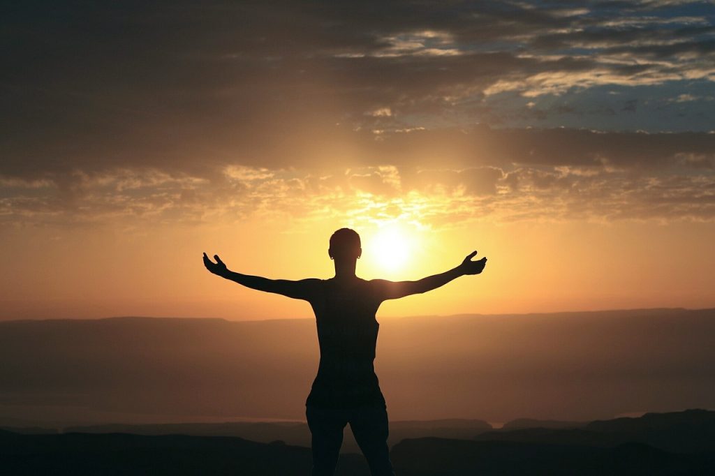 Silhouette of a person standing with arms outstretched against a sunset sky.