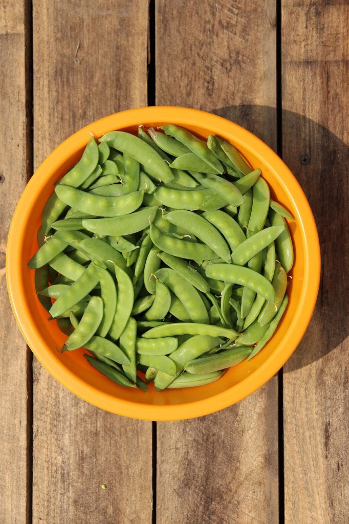 A bowl of fresh green snap peas on a wooden surface.