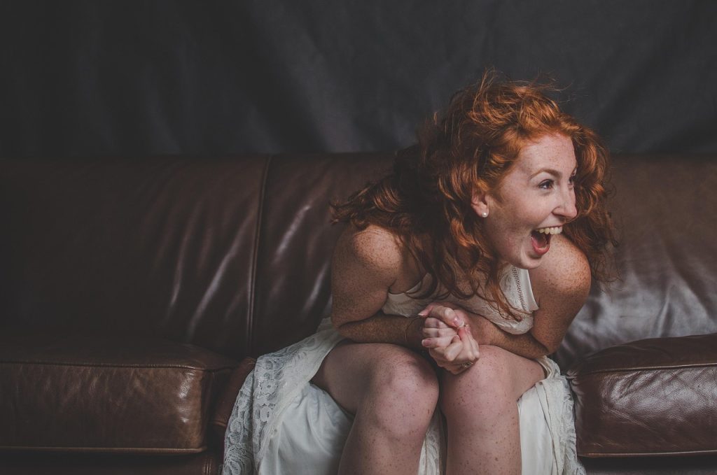 A woman with red hair laughing while sitting on a leather sofa.