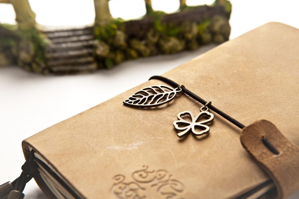 A leather-bound journal with leaf and clover charm bookmarks.