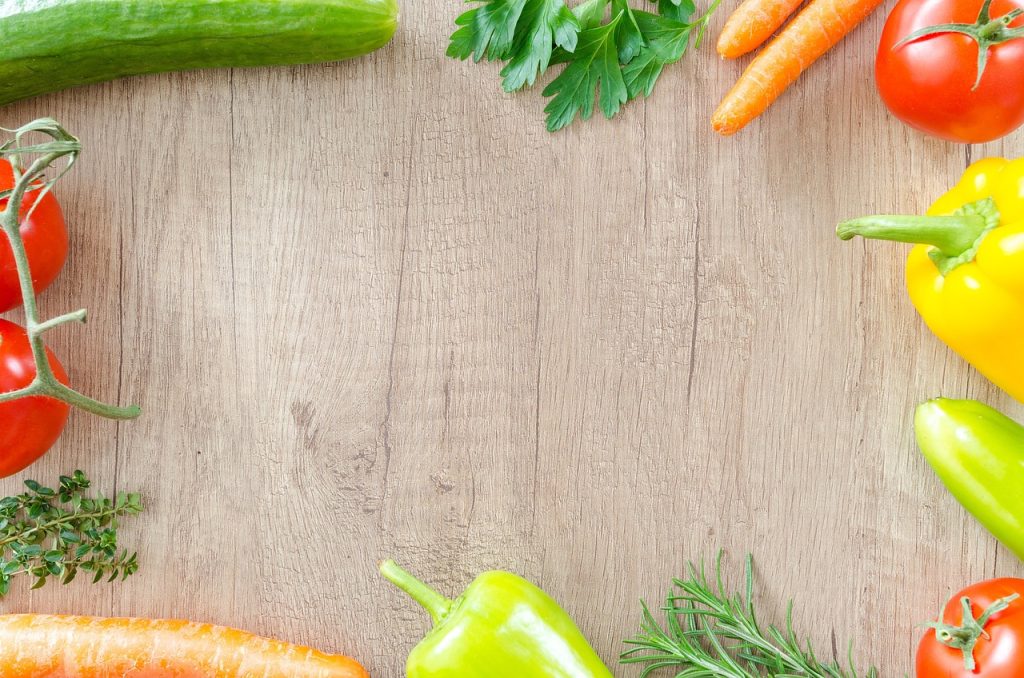 Fresh vegetables and herbs arranged around a wooden board.