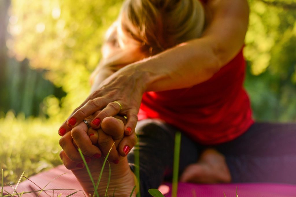 A woman stretching toward her foot on a yoga mat outdoors in golden light.