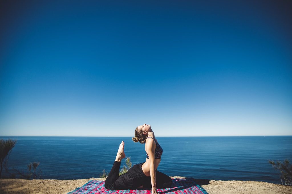 Woman practicing a yoga backbend on a mat overlooking the ocean.