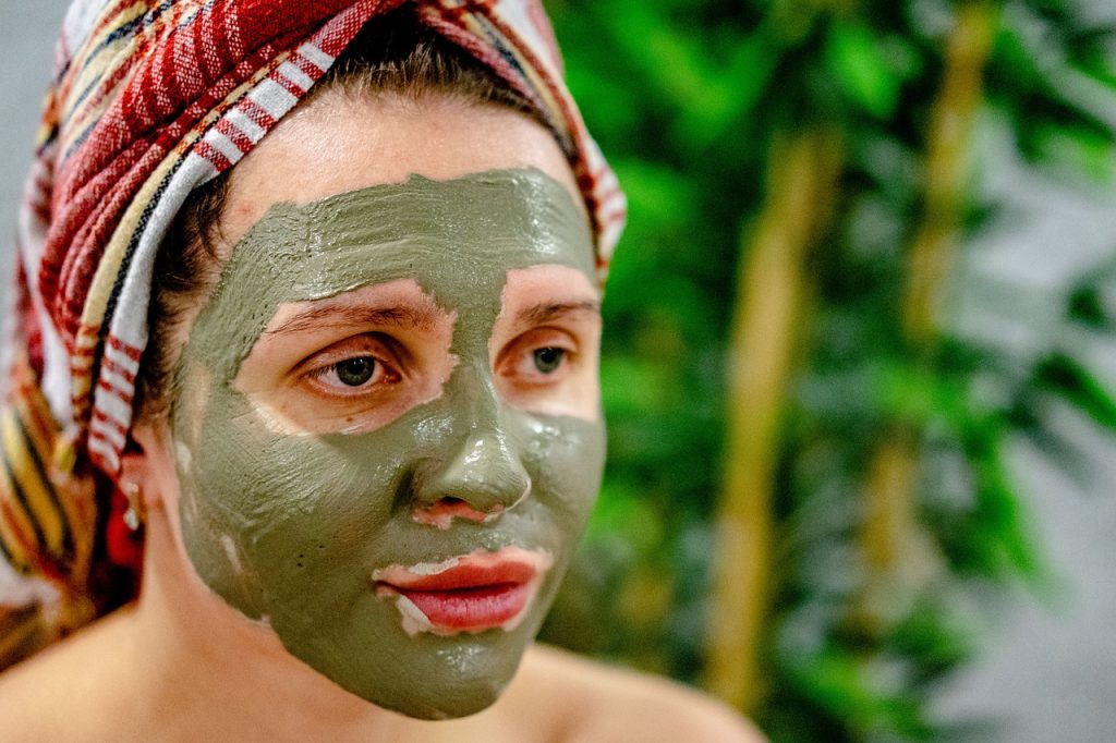 Woman with a green clay face mask and a towel wrapped around her hair.