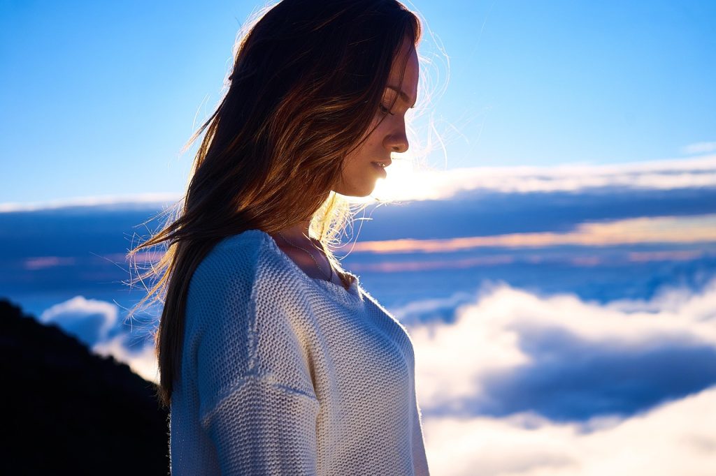 Woman standing above the clouds at sunset with her eyes closed.