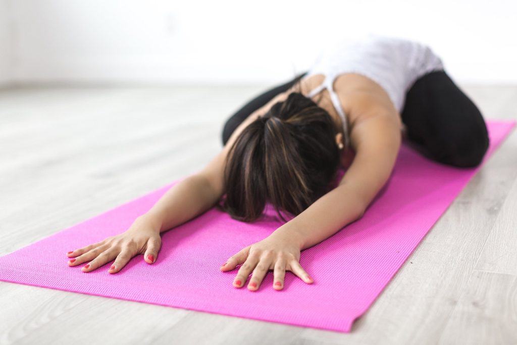 Woman resting in child's pose on a pink yoga mat.