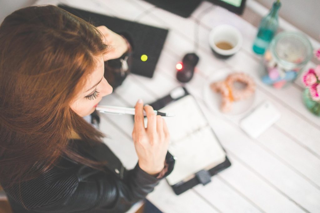 A woman in a leather jacket holding a pen over an open planner at a white table with a coffee cup.