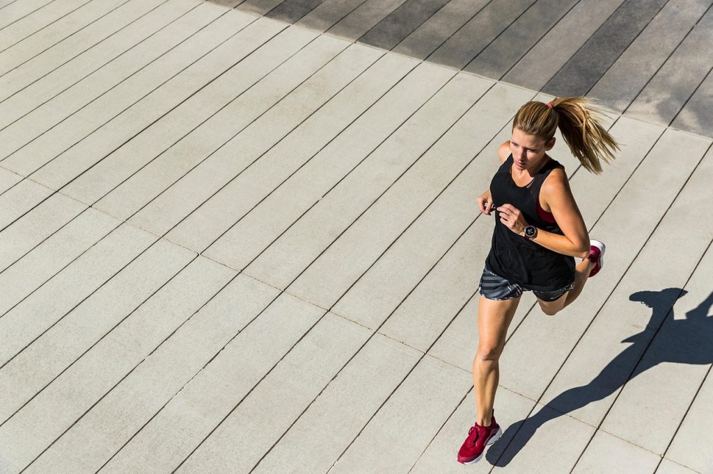 A woman running outdoors on a paved surface, seen from above, casting a long shadow.