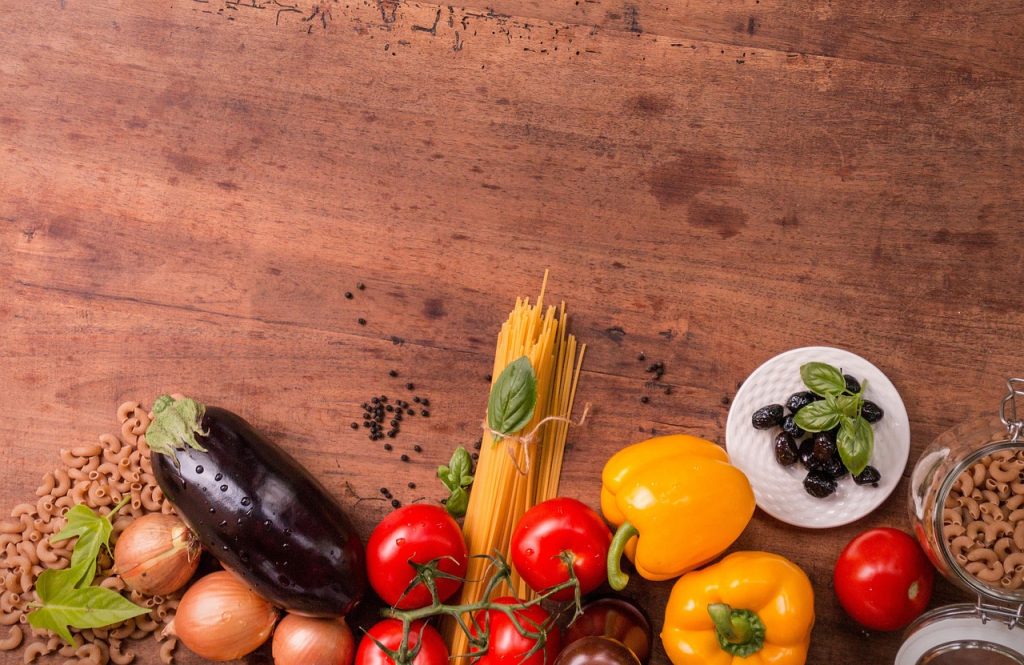 Fresh vegetables and dried pasta arranged on a wooden surface.