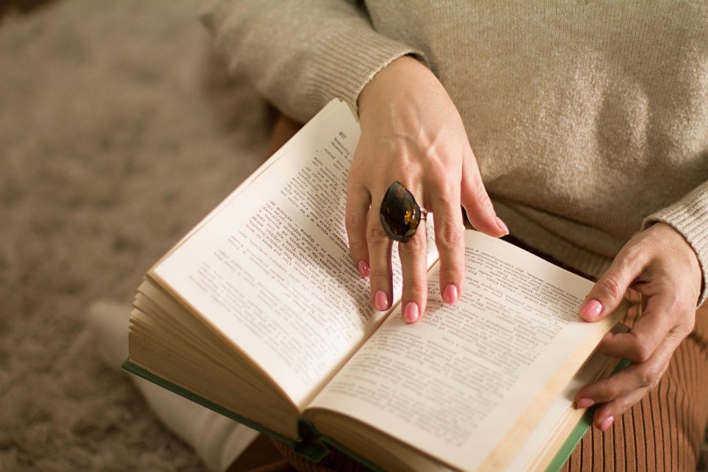 A woman holding an open book, reading it on her lap.
