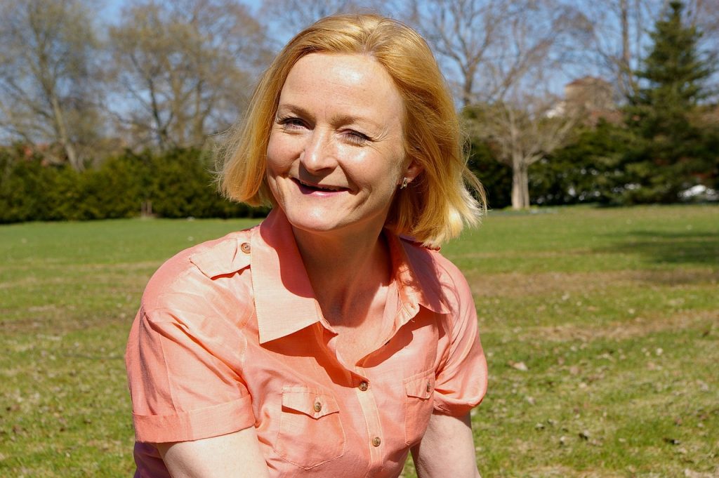 A smiling woman sitting outdoors in a green park.