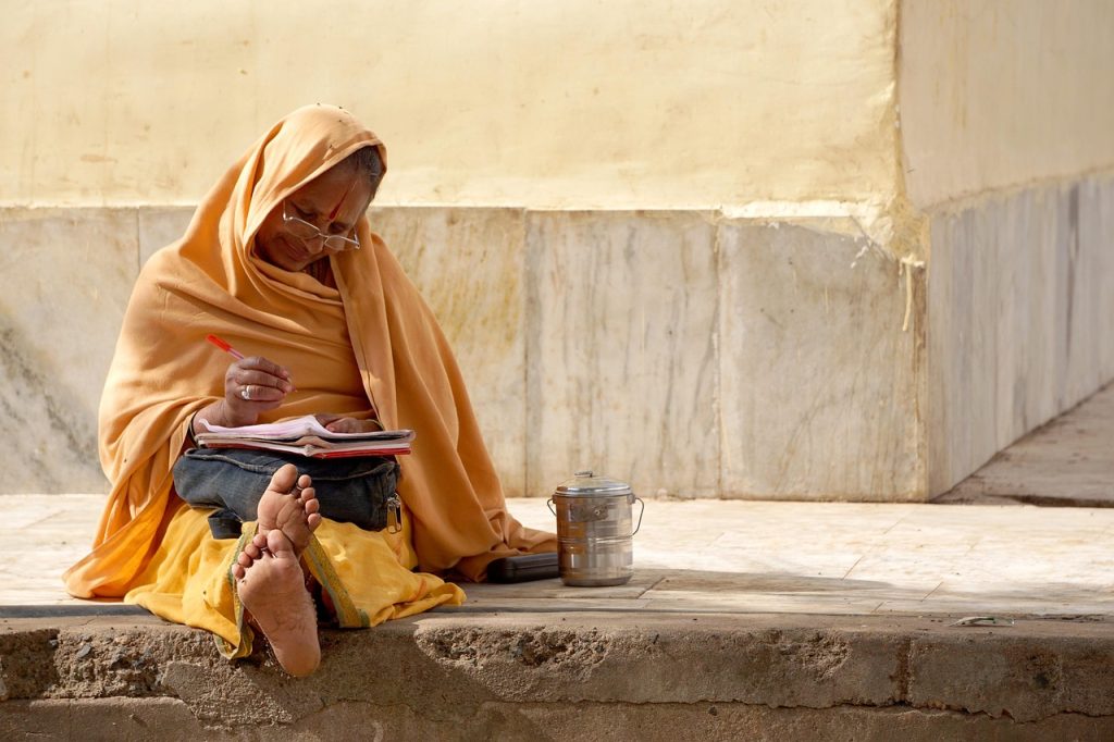 A woman in a yellow outfit reading and writing while sitting on stone steps.