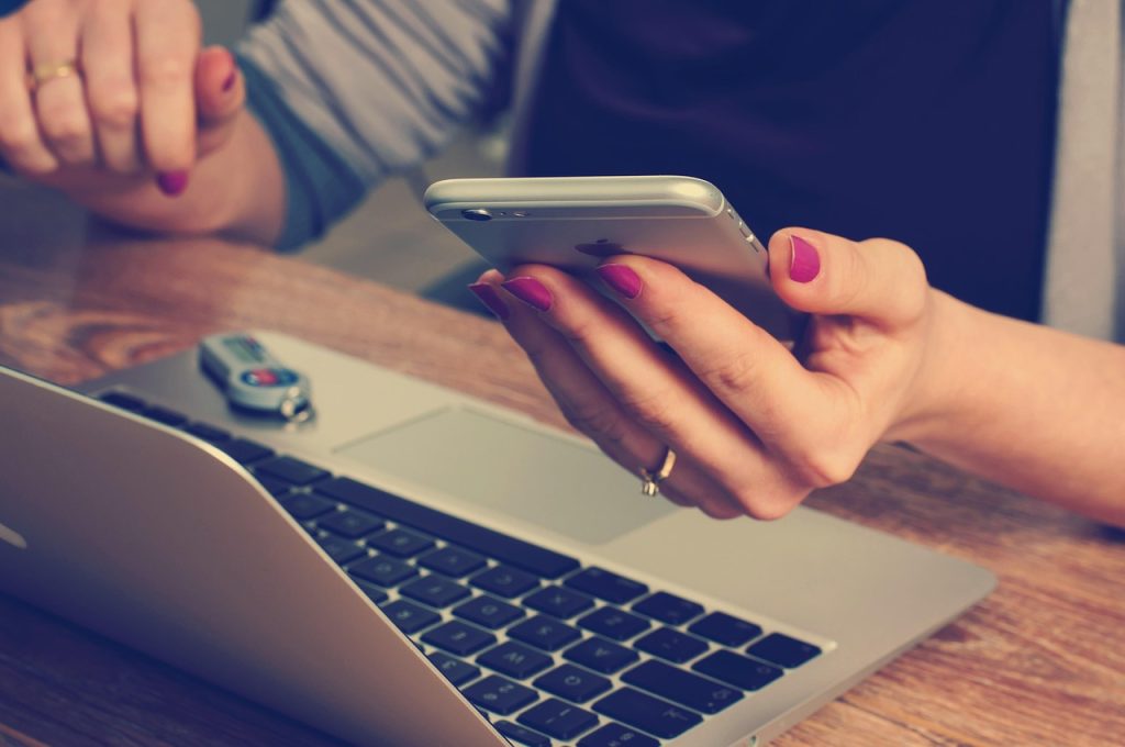 A woman's hands holding a phone above a laptop keyboard.