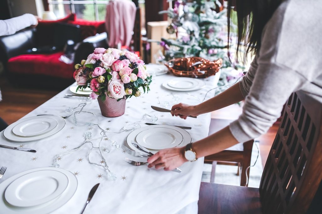 A woman setting a table with a meal and flowers.