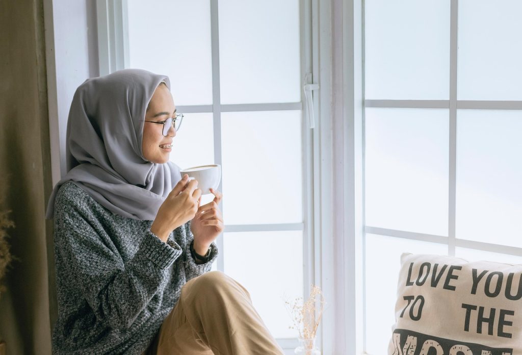 A woman sitting by a window holding a mug.